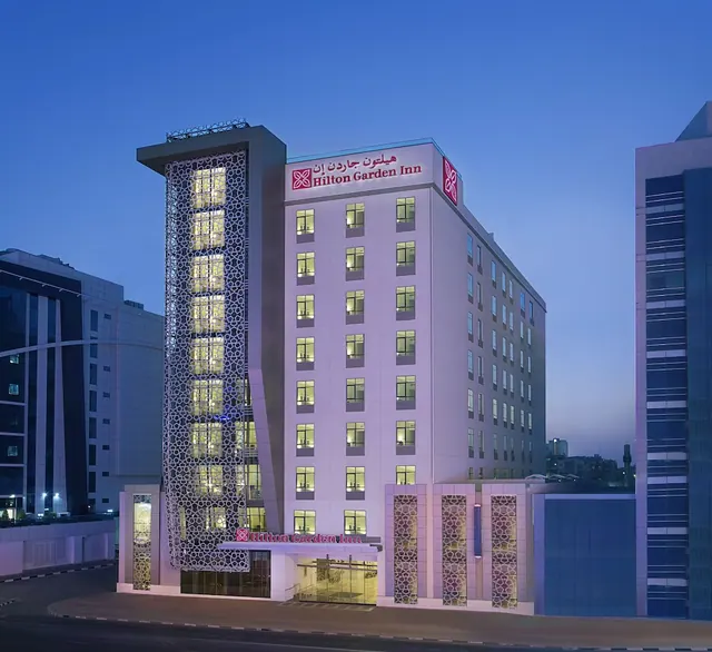 The exterior of a Hilton Garden Inn hotel building at dusk, with illuminated windows and entrance signage.