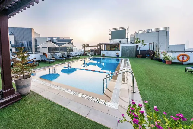 A rooftop swimming pool with sun loungers, white parasols, a lifebuoy and a small bar area under a hazy sky.