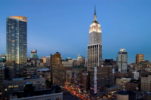 Elevated dusk view over Midtown Manhattan toward the illuminated Empire State Building, with office towers and street traffic below.