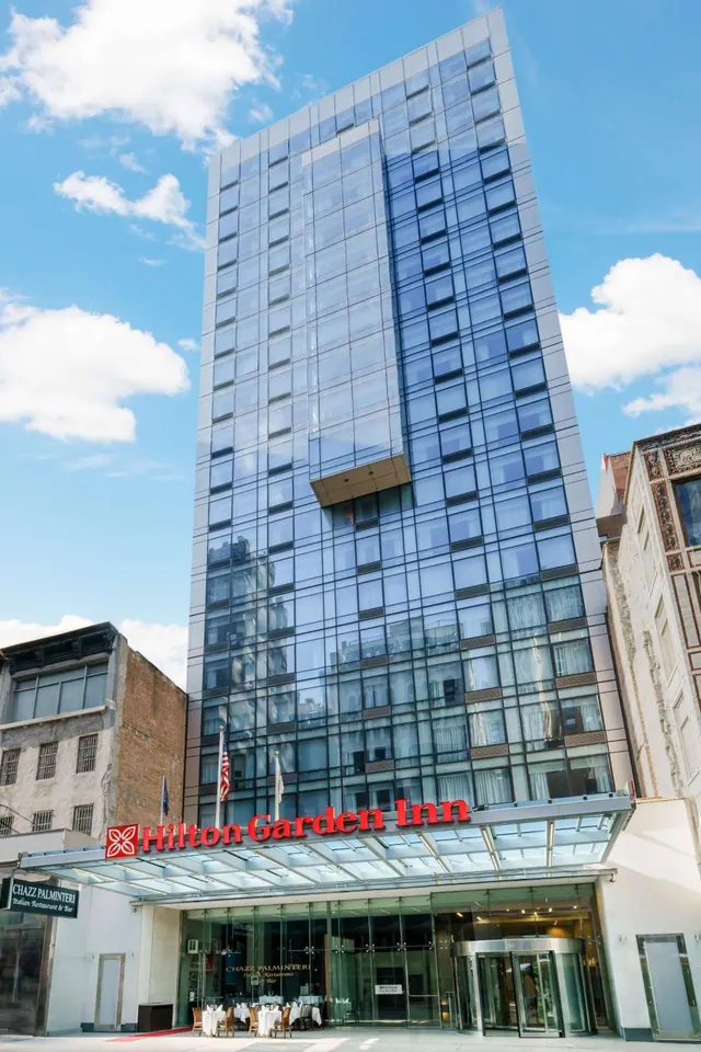 Exterior view of a tall glass-fronted hotel tower with a Hilton Garden Inn sign above a covered entrance canopy.