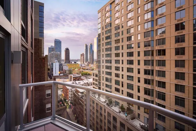 A view from a private balcony over a city skyline and neighbouring brick and stone apartment buildings at dusk.