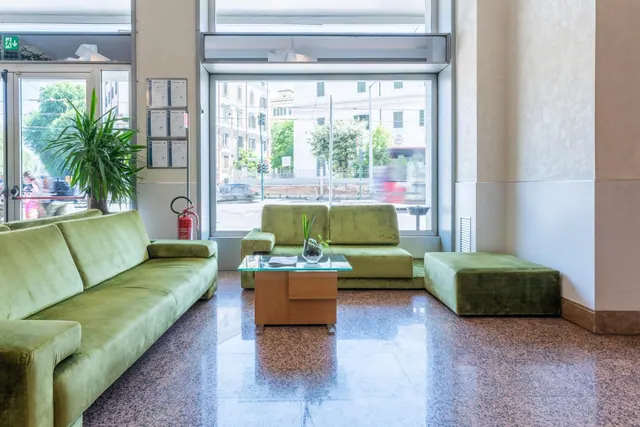 A lobby seating area with green velvet sofas and a glass-topped coffee table, with a large window looking onto a street outside.
