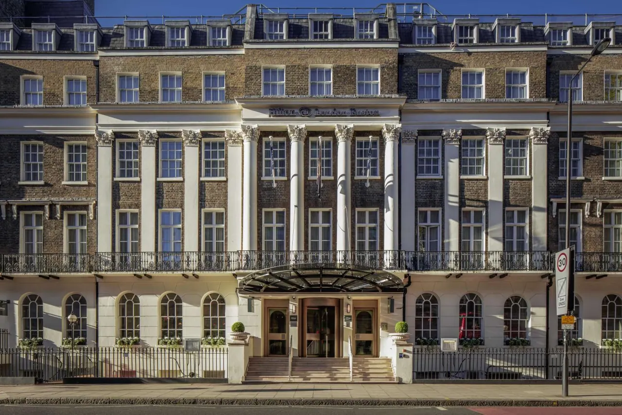 The front facade of a brick hotel building with white classical columns, a central entrance canopy, and steps leading up to the doors.