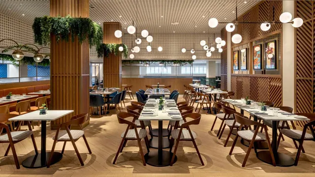 A restaurant dining room with wooden columns, globe pendant lights, and rows of tables set with place settings and upholstered wooden chairs.