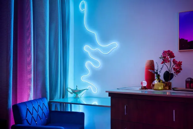 A hotel room with a glowing neon wave light installation on the wall, a blue tufted velvet armchair, a dresser with orchids and vases, and a genie lamp on a small glass table.