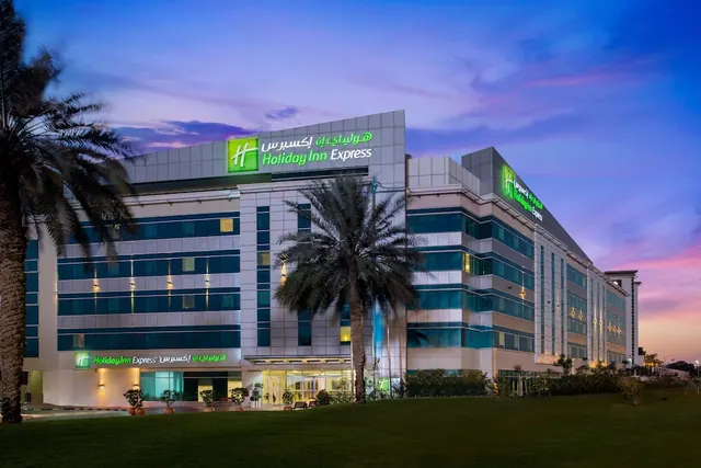 Exterior of a Holiday Inn Express hotel building at dusk, with palm trees and a grass lawn in front.