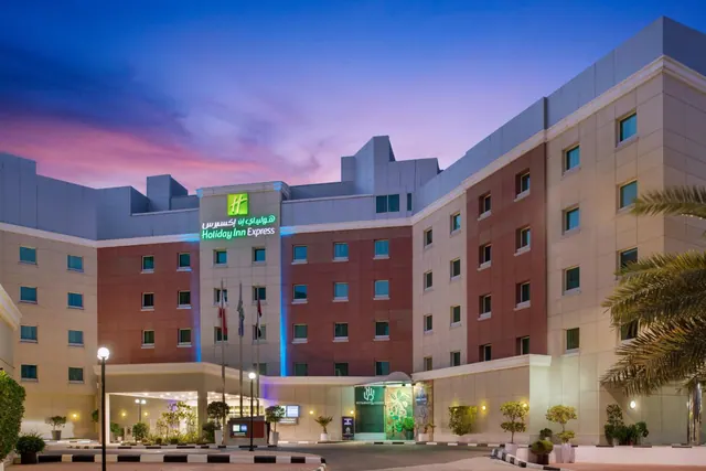 Exterior of a Holiday Inn Express hotel building at dusk, with illuminated signage, lit windows and a covered entrance portico.