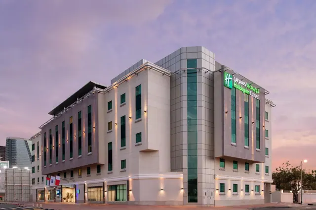 Exterior of a Holiday Inn Express hotel building at dusk with illuminated windows and a street in front.