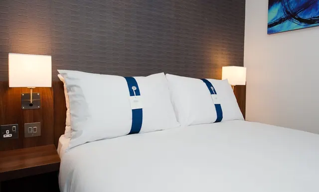 A made double bed with white linen and blue-banded pillows sits beside two wall-mounted bedside lamps.