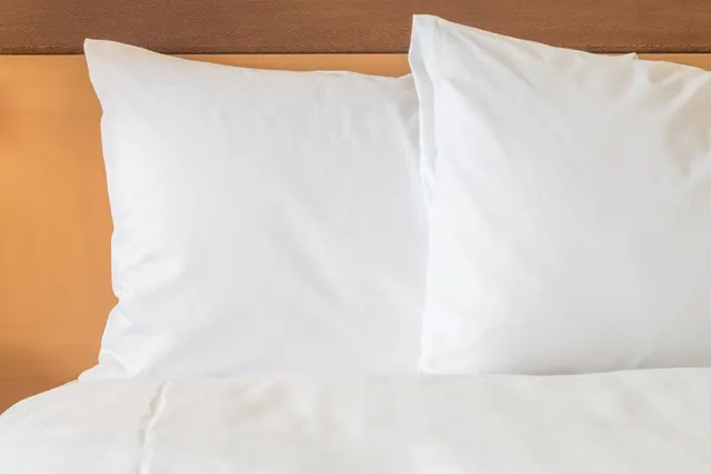 Two white pillows and a white duvet on a bed with a wooden headboard.