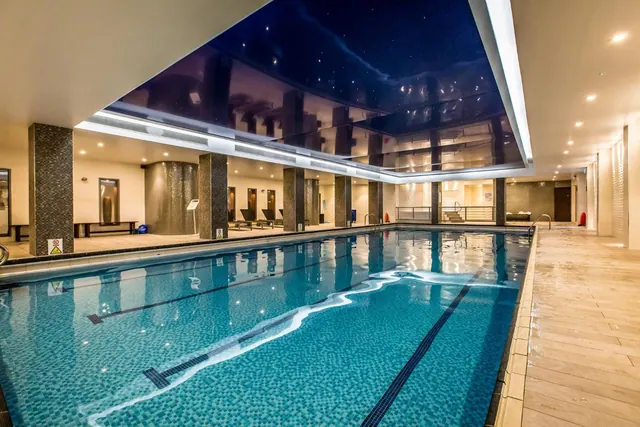 An indoor lap pool with lane markings, a dark ceiling with small lights, tiled pillars and sun loungers in the background.