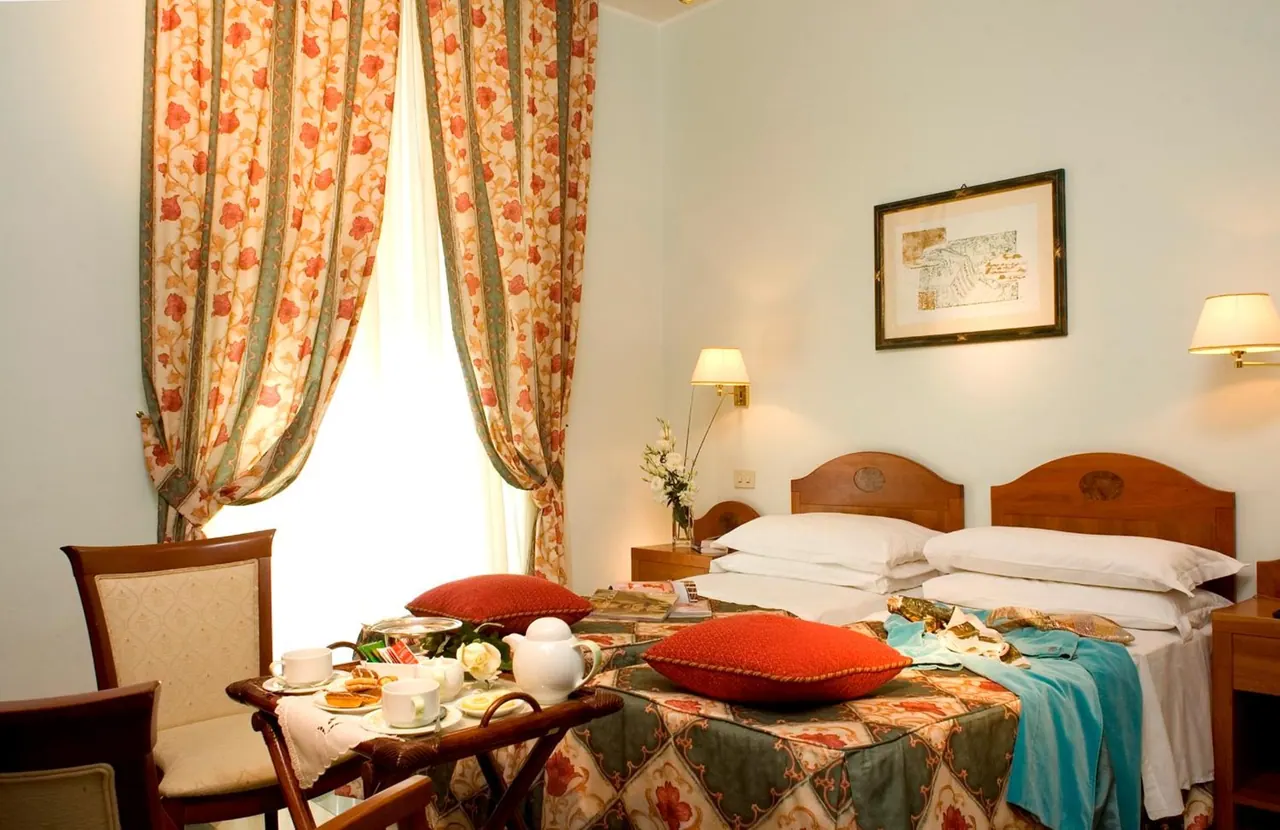 A bedroom with two beds under a framed picture, floral curtains at the window, and a tea tray with cups and pastries on a small table.