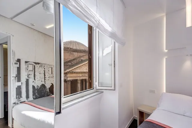 A bedroom with twin beds and an open window showing the dome and facade of the Pantheon.