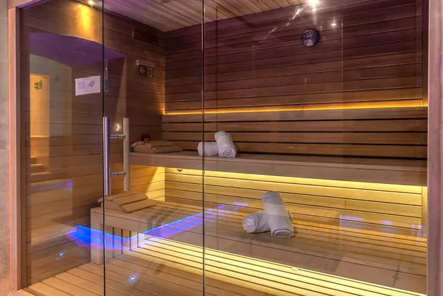 A wooden sauna cabin with a glass door, warm underlit benches and rolled white towels on the seats.