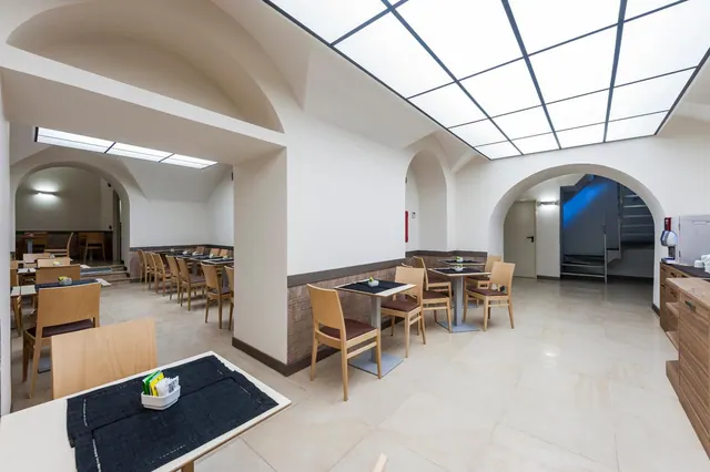 A dining room with arched ceilings and a skylight, with wooden chairs at small tables set with dark placemats and a wooden counter along the right wall.