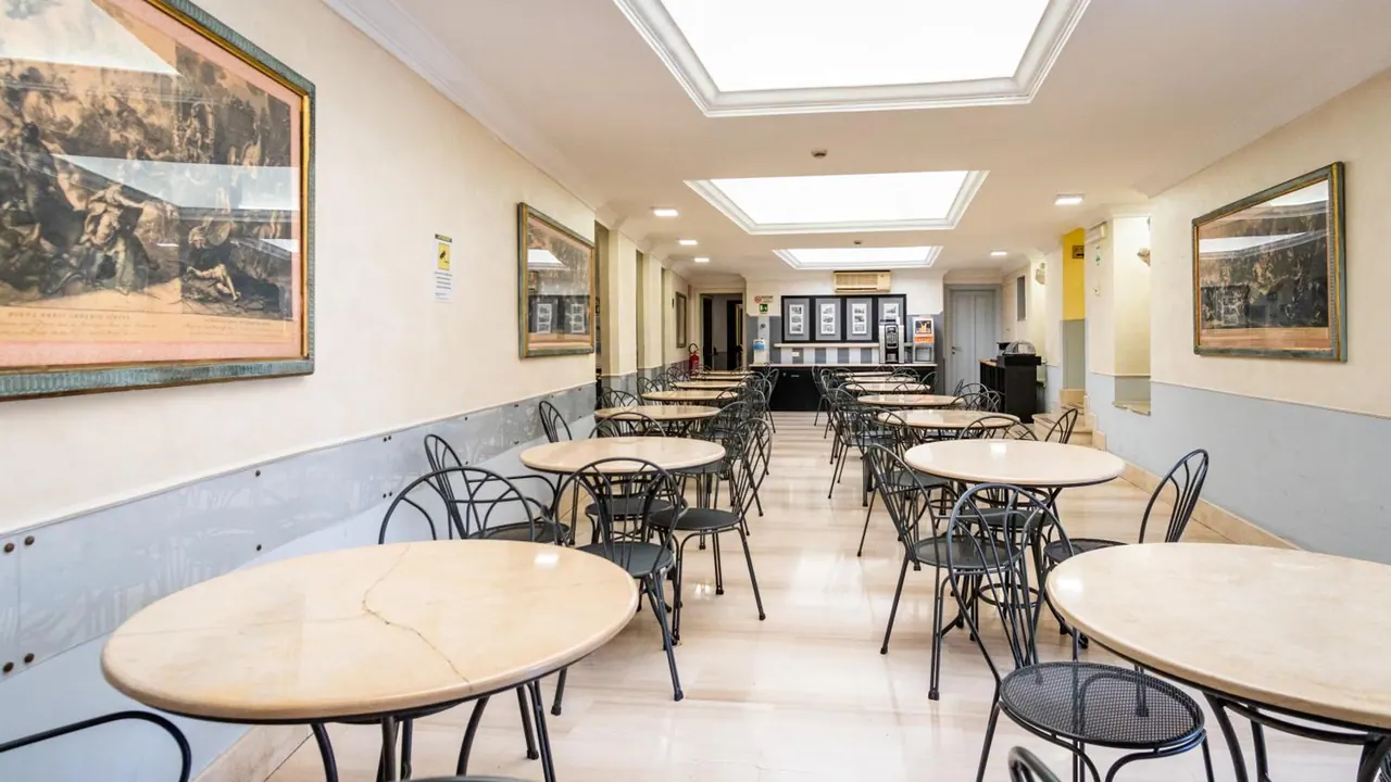An empty dining room with round marble-top tables, black metal chairs, framed prints on the walls and skylights in the ceiling.