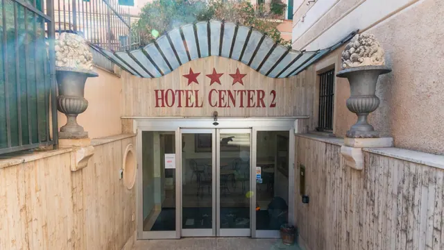 The entrance of Hotel Center 2 with red star symbols above the sign, glass doors, and stone urns on pillars on both sides.