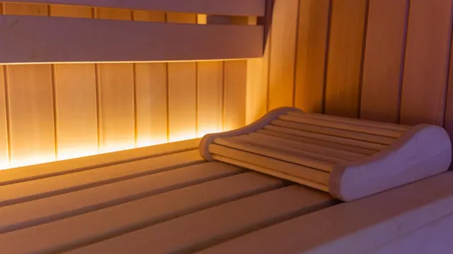 A wooden sauna bench with a slatted wooden headrest, lit by a warm light strip along the lower wall.