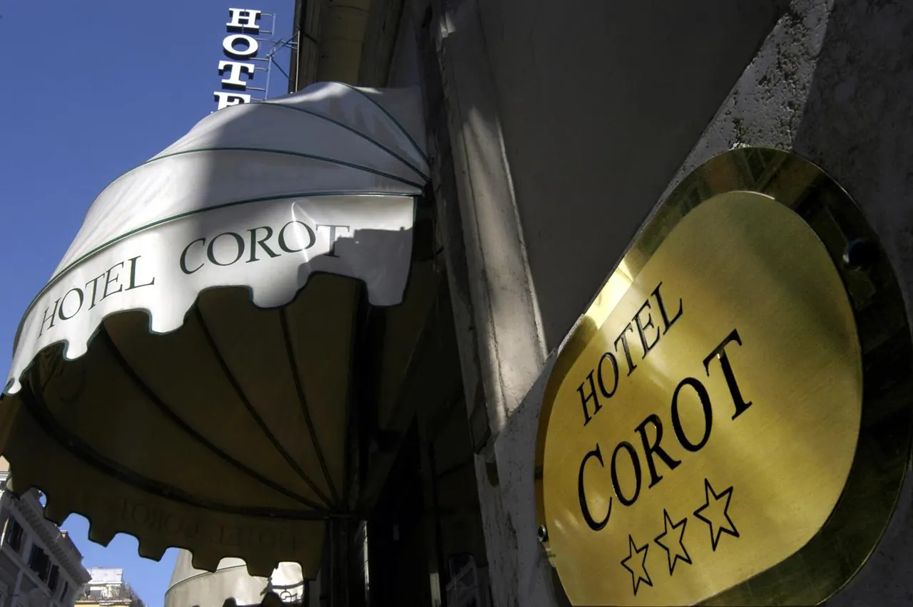 Exterior of Hotel Corot showing a white awning printed with the hotel name, a gold plaque reading Hotel Corot with three stars, and a vertical hotel sign on the building above.