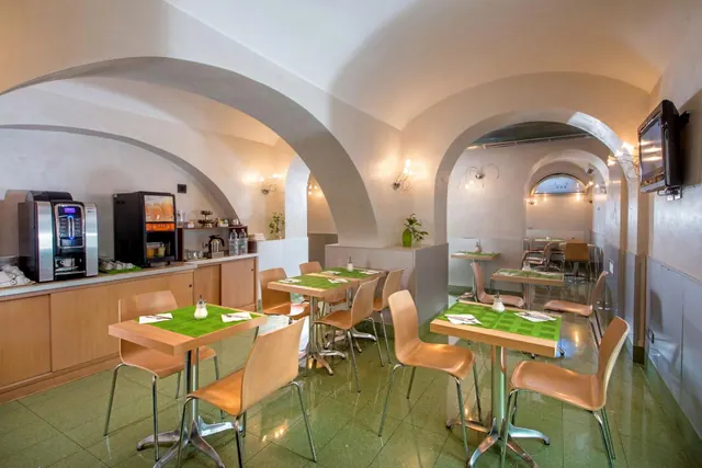 A breakfast room with vaulted arched ceilings, tables set with green placemats, and coffee machines on a wooden counter at left.