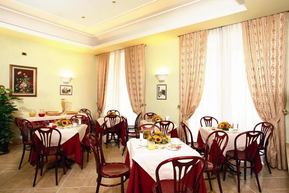 A breakfast room with tables covered in red and white linen, sunflower centrepieces, dark wooden bentwood chairs and tall curtained windows.