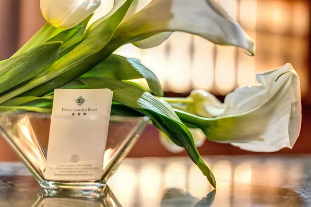 White calla lilies stand in a glass bowl on a glossy table beside a stack of paper napkins printed with the Flower Garden Hotel logo.