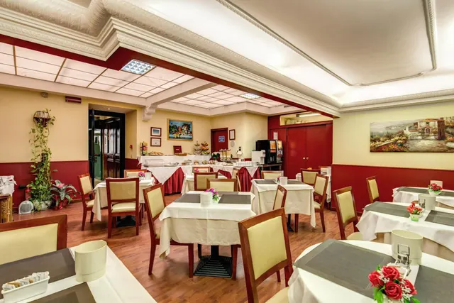 A breakfast dining room with white-clothed tables, upholstered wooden chairs, a buffet counter in the background and a landscape painting on the wall.