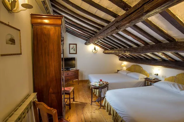 A bedroom with two beds under exposed wooden ceiling beams, with a wooden wardrobe, a television on a dresser, and a small table holding a tray.