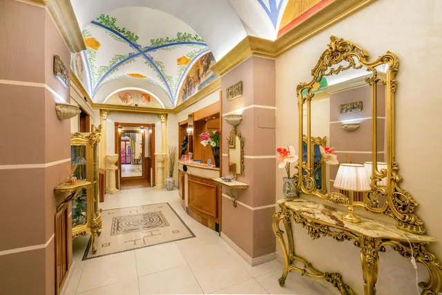 A lobby corridor with a painted vaulted ceiling, a gilded mirror and marble console table, and a reception desk in the background.
