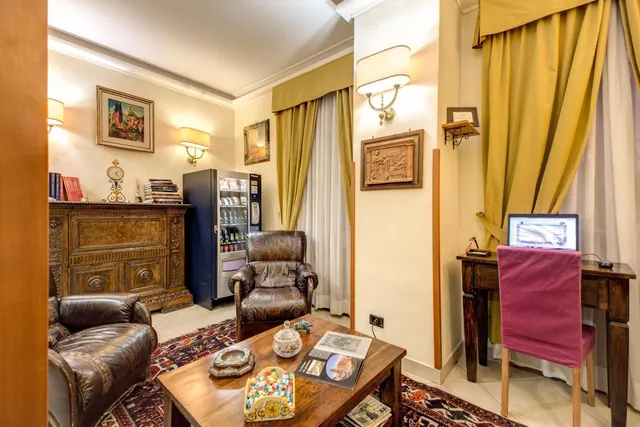 A sitting area with two leather armchairs, a wooden coffee table, a vending machine, and a desk with a laptop beside a window with yellow curtains.