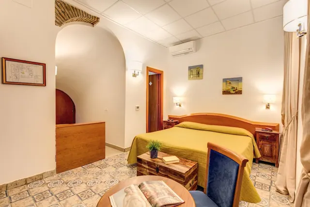 A bedroom with a double bed under a yellow bedspread, a wooden headboard, bedside tables, a wall-mounted air conditioner and an arched doorway.