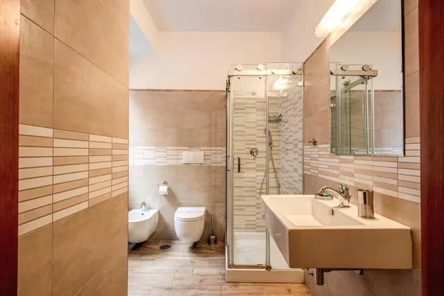 A bathroom with a wall-hung basin, a bidet and wall-mounted toilet, and a glass-enclosed walk-in shower with a hand shower.