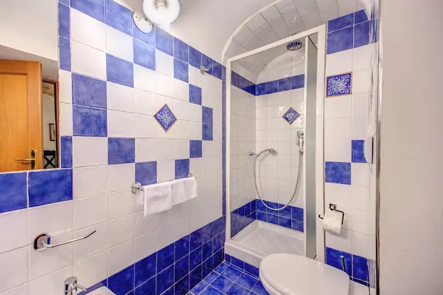 A tiled bathroom with blue and white walls, a walk-in shower with a glass door, a toilet, and white towels hanging on a wall rail.
