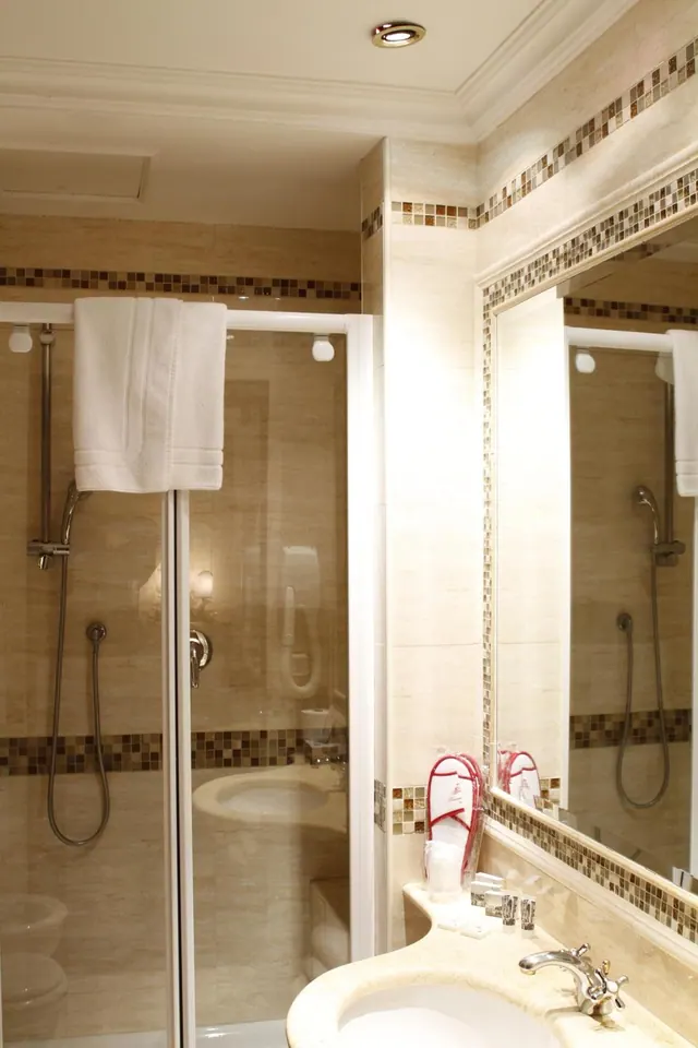 A bathroom with a glass-enclosed shower, a white towel hung over the screen, a mirror framed in mosaic tile, and a sink with a chrome tap.