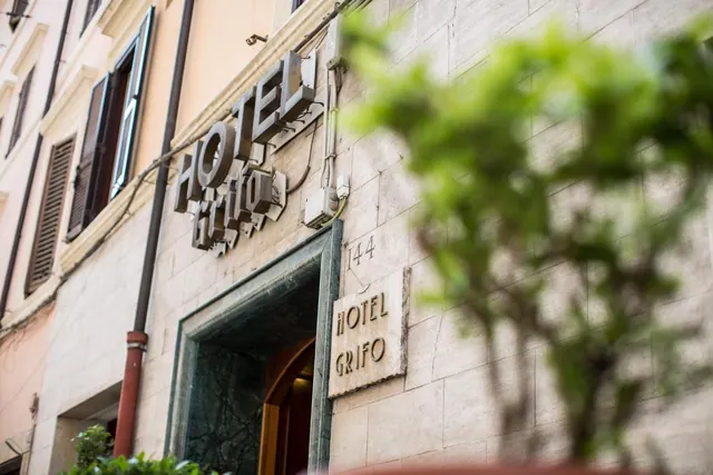 The stone facade of Hotel Grifo, with its raised sign, a marble-framed doorway and a plaque beside the entrance, with a blurred plant in the foreground.
