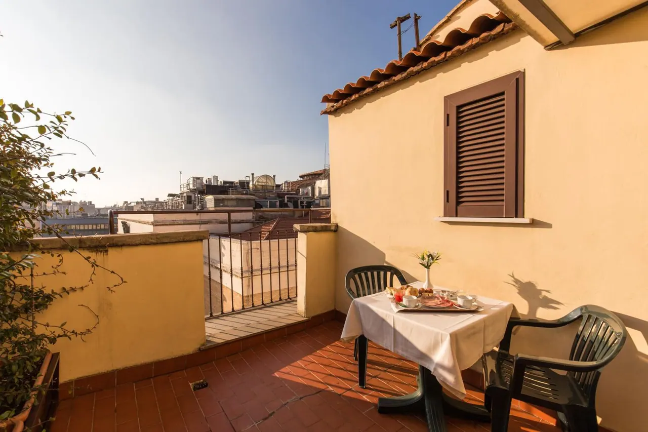 A tiled terrace with a set breakfast table, two green chairs and a view over rooftops and a dome.
