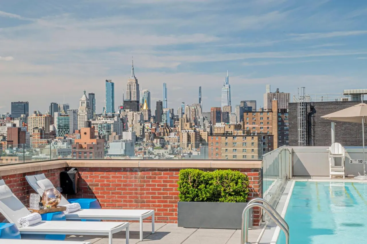A rooftop pool with sun loungers and a shade umbrella, with the Manhattan skyline and the Empire State Building in the background.