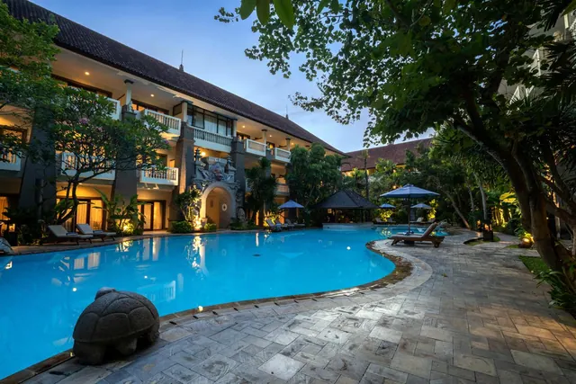 A large kidney-shaped swimming pool at dusk with sun loungers, umbrellas and a stone turtle sculpture beside the hotel building.