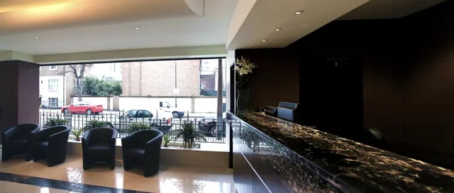 A lobby with black armchairs by a large street-facing window, with a dark marble reception counter on the right.