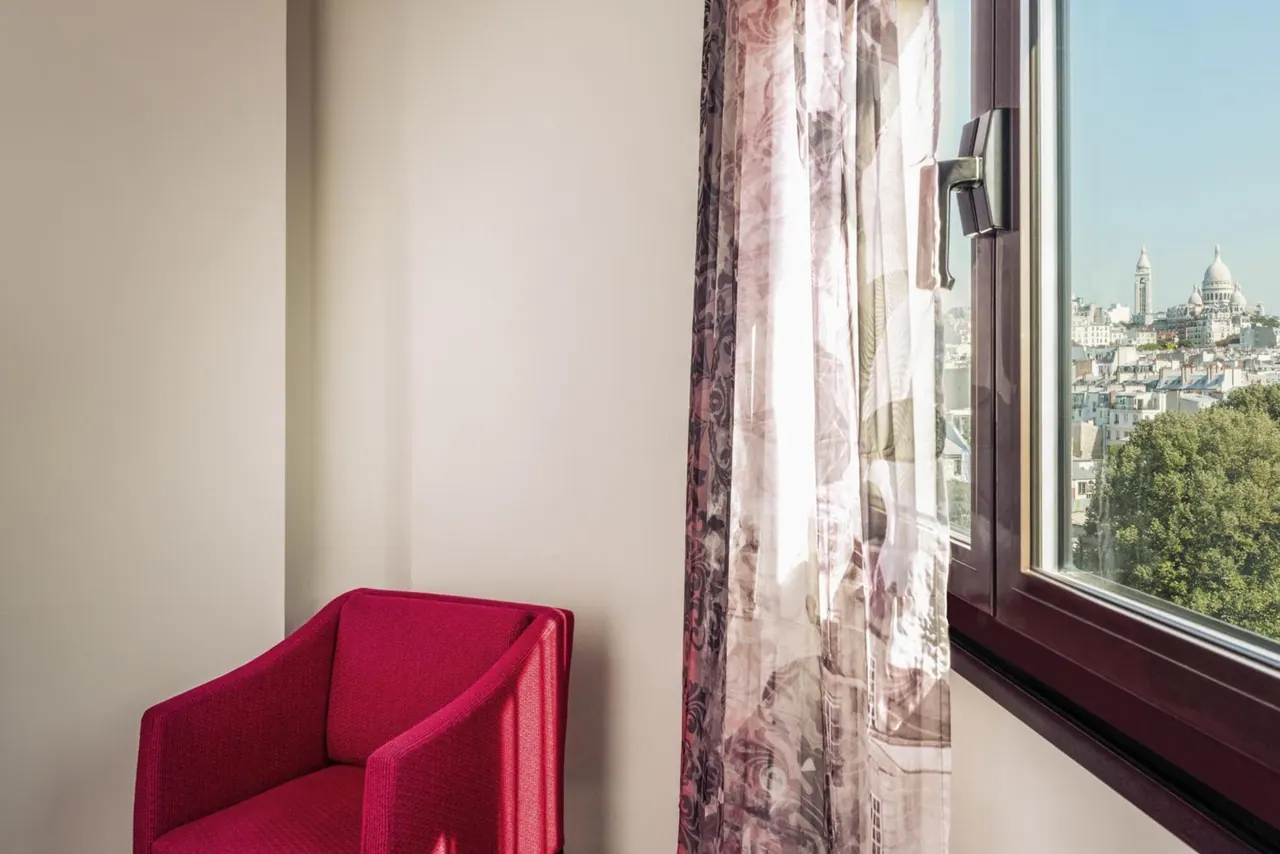 A red armchair sits beside a window overlooking Paris and the Basilica of Sacré-Cœur.