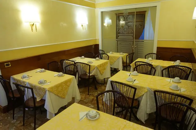 A breakfast dining room with yellow patterned tablecloths, set tables with cups and saucers, dark wood wall panelling and wall lights.