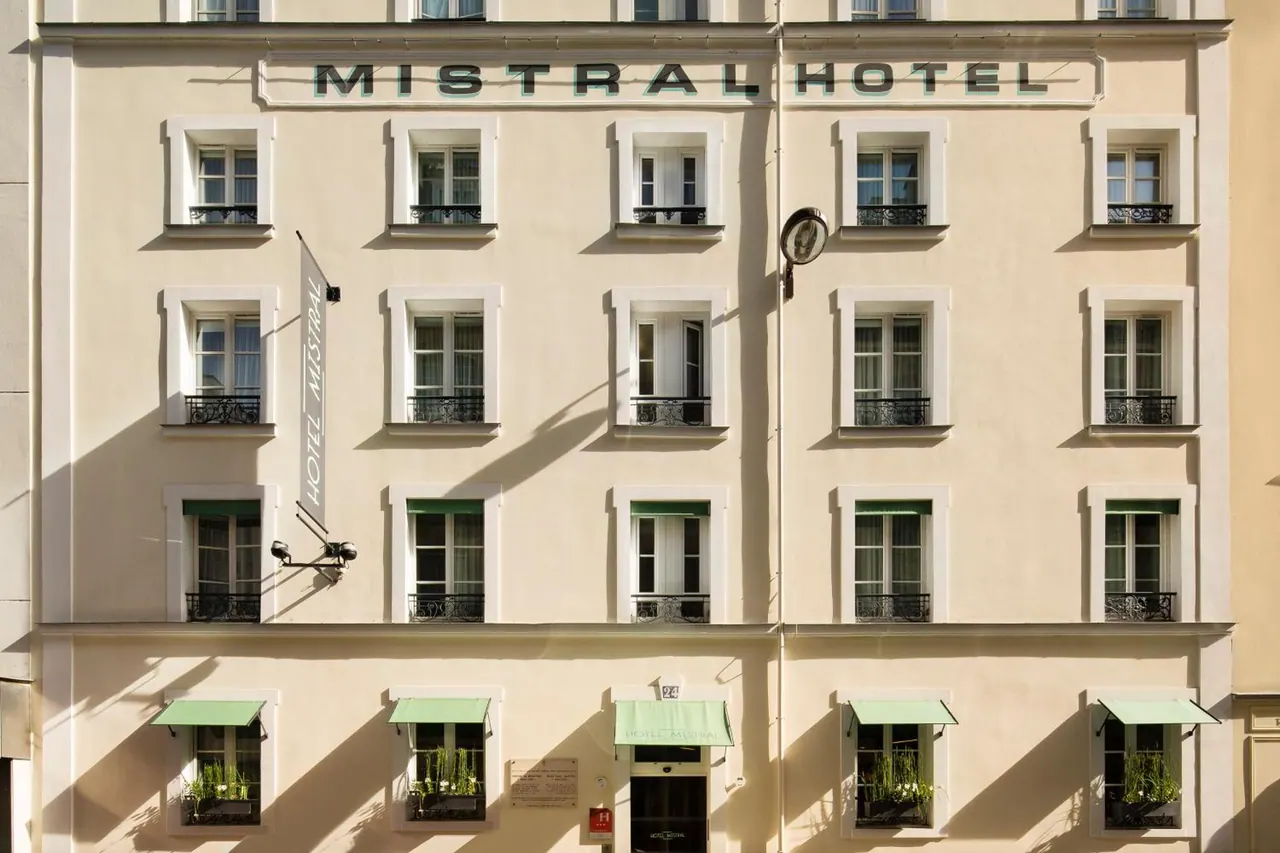 The Mistral Hotel facade has cream-colored walls, rows of windows, green awnings, and decorative balconies.