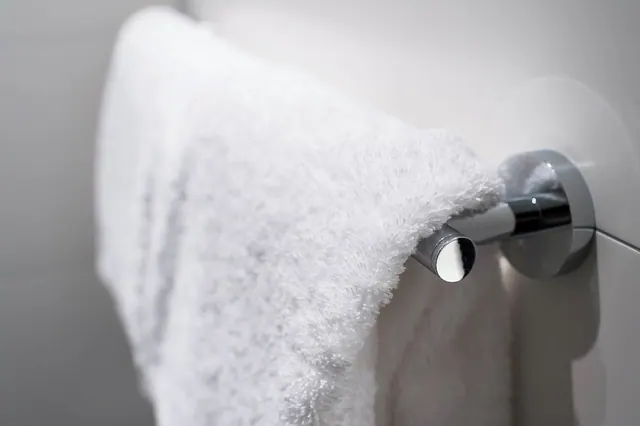 A white towel hangs over a chrome towel bar against a plain white wall.