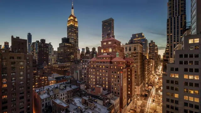 Twilight view over Midtown Manhattan rooftops and streets toward the illuminated Empire State Building.