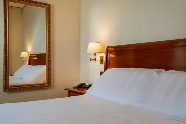 A double bed with a wooden headboard, wall-mounted lamps, a gold-framed mirror and a telephone on a bedside table.