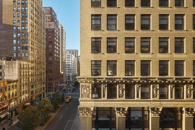 View from an upper floor looking down a city street lined with tall brick buildings and yellow taxis.
