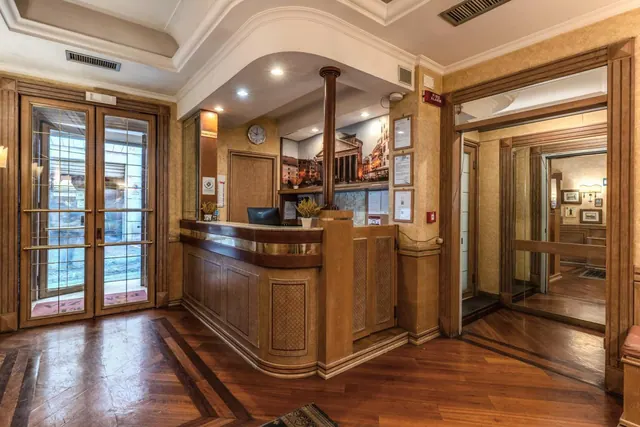 A wooden reception desk stands in a lobby with a framed Rome photo mural behind it, glass double doors on the left, and an open lift on the right.