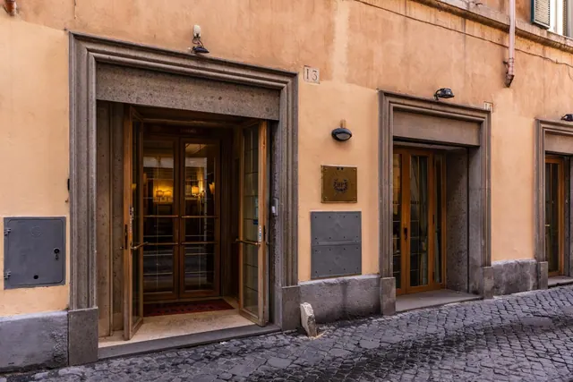Street-level facade of an ochre building with stone door surrounds, glass double doors, a brass plaque and the number 13, above cobbled paving.
