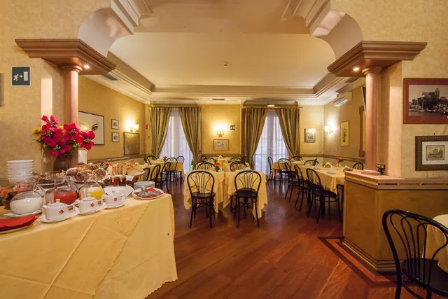 A breakfast dining room with set tables, bentwood chairs, and a buffet with pastries and drinks on the left.