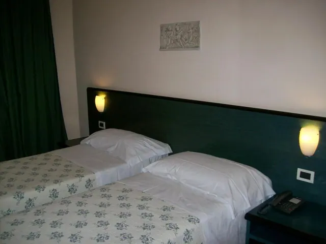 Two single beds with floral bedspreads and white pillows sit beside a dark green headboard with wall lights, and a telephone sits on the nightstand.